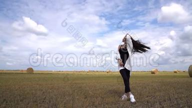穿着黑色休闲服的漂亮黑发女孩站在田野里，手里拿着一堆圆圆的干草堆，直着她的头发